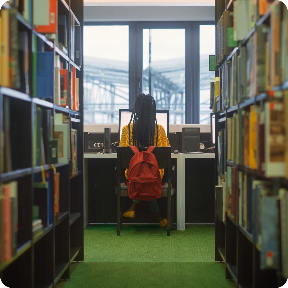 A person diligently working at a desk in a library setting.